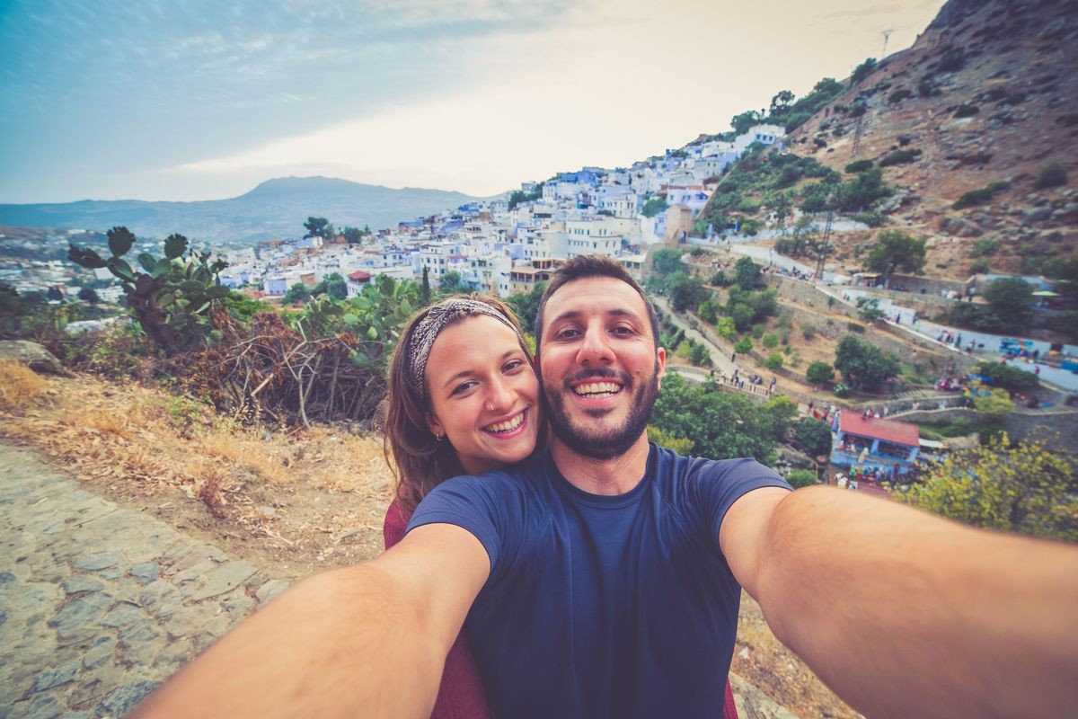 Happy young tourist backpackers couple taking selfie on a street in Medina with the blue town of Chefchaouen in background, Morocco during Africa tour